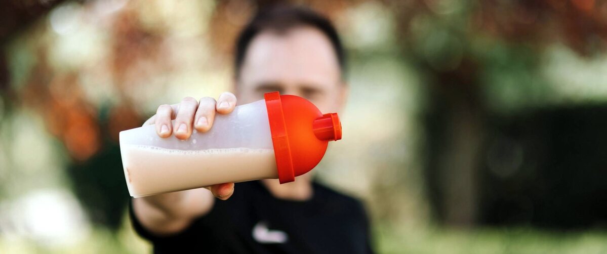 a guy holding a protein shake in a sport shaker with a blur background